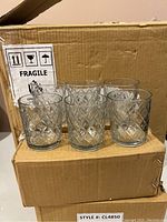 Six clear glass votive candle holders with a diamond pattern, arranged on top of a cardboard box.