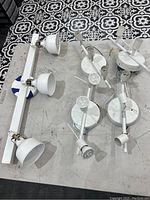 Overview of five white ceiling light fixtures including a triple spotlight bar and four round base spotlights laid out on floor.