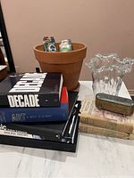 Overview of lot with stacked coffee table books, terracotta planter, glass vase, moisture readers, and trinket box