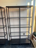 Front view of black metal frame shelving unit with glass shelves and solid bottom shelf, showing overall size and condition.