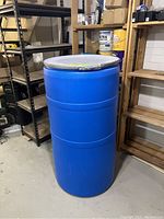 Full view of the large blue plastic barrel drum standing upright, showing its size and cylindrical shape.