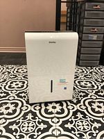 Front view of white Danby dehumidifier on patterned black and white floor showing logo and water level indicator window.