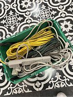 Top view of green bin containing various coiled extension cords including yellow and green cords with a white power bar on top.
