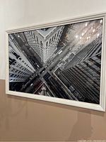 Framed black and white photo print showing tall buildings and streets in downtown Toronto from a high angle, with reflections of chandelier lights on the glass.