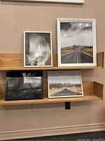 Four framed photographic prints displayed on two wooden shelves against a wall, showing urban and road landscape images.