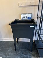 Front view of black plastic laundry tub standing on tiled floor.