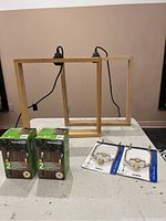 Photo showing the lot contents on a table: two boxed solar lights, two oak hanging pendant light frames, two brass lamp harp kits on their packaging.