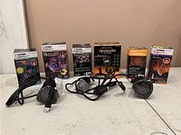 Five Halloween-themed LED projection lights displayed with their original boxes, showing light effects like twirling colors, ghost flames, and star patterns