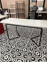 Full view of black metal table base holding a white marble-like rectangular table top, showing the base structure and leg design on patterned tile floor.