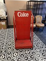Front view of red metal dolly/cart with "Enjoy Coke" logo on back panel. Showing wear and surface rust.