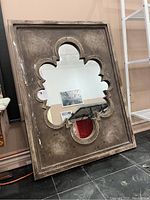 Full view of mirror showing wooden frame with distressed finish and ornate cutout glass in center