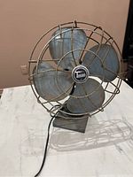 Front view showing four metal blades with worn blue paint, rusted wire cage and corded base with Torcan logo on the hub.