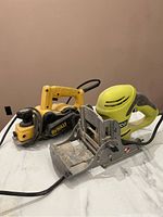 Photo showing yellow and black DeWalt wood planer alongside lime green Ryobi biscuit jointer on a white surface.
