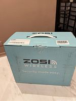 Blue box labeled ZOSI Wireless Security System main packaging with handle on top, showing brand and tagline 'Security made easy.'