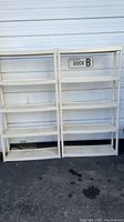 Two white plastic outdoor storage racks side by side against a white metal wall with a Dock B sign above.