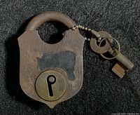 Front view of antique unbranded padlock showing round brass keyhole cover and attached key on ball chain