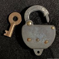Closed padlock next to the key on a black background, showing overall shape and size.