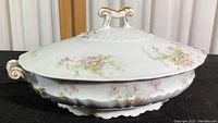 Closed view of the white porcelain covered dish showing floral design, gold trim, and handles.