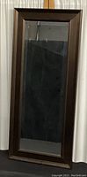 Full view of the tall rectangular mirror showing the bronze tone wooden frame and reflective beveled glass surface.