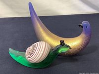 Photo showing both glass snail figurine with green body and striped shell and textured gold finish bird figurine with gradient coloring.
