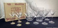 Wine rack and multiple martini glasses with beverage carafe on a dark cloth, carafe visible with looped glass