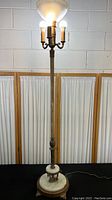 Full view of tall vintage floor lamp with onyx base, metal stem, and candelabra style bulb holders with glass shade on top