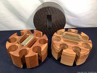 Two wooden poker chip holders, one with a metal handle and one without, shown alongside a textured cover on the felt base.