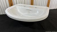 Front view of white porcelain countertop sink, showing glossy finish and rounded shape.