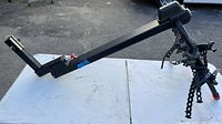 Side view of black metal bike hitch rack laid horizontally on a white table outdoors, showing the main arm and arms for bike attachment points with chains at ends.