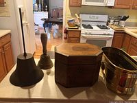 Photo showing the two bells, wooden box and brass bucket on a kitchen counter