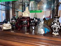 Wide shot showing white porcelain Buddha seated on wooden stand, metal bird sculpture, porcelain box with gold decoration, and black and white floral vase.