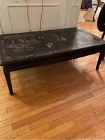 Full view of the black carved Asian coffee table showing its rectangular shape and detailed top surface artwork.