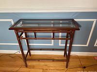 Front view of the console table showing glass top and wooden frame with bamboo-style design.