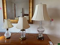 Full view of three crystal lamps on wooden surface under mirror; varying sizes and lampshades visible.