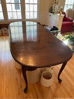 Long wood dining table with cabriole legs from a side angle, showing two leaves extended and part of room in background.