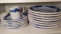 Stack of dinner plates, lunch plates, and mugs featuring blue fish motifs and a white base with visible crazing.