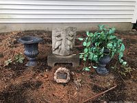 Three outdoor stone garden items including two planters and a cherub statue on low block, plus a small stone-like base solar light in front.