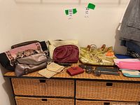 Photo showing multiple handbags, purses, clutches, sunglasses, and small pouches arranged on a wicker chest.