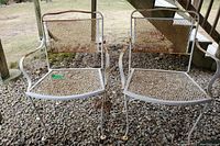 Pair of metal patio chairs shown together, displaying mesh seat and back with rust and enamel loss, outdoor setting on gravel.