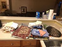 Wide shot of folded assorted table linens including placemats, table runners, napkins, and oven mitts laid out on a kitchen counter.