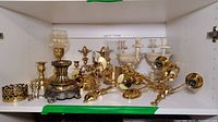 Shelf display of multiple brass and metal decorative pieces including sconces, candle holders, a wall pocket, and cast iron centerpieces.
