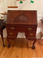 Full front view of antique claw foot secretary desk showing carved fan panel, brass hardware, and wooden finish.