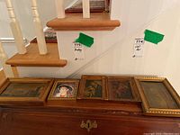 Five framed vintage artworks displayed on a wooden surface beneath a staircase, showing the variety of sizes and frame styles.