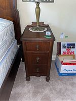Front view of antique wood side table with three drawers and lamp on top