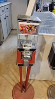 Full view of floor-standing metal candy dispenser with red legs and clear plastic hopper