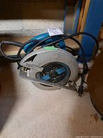 Makita circular saw on floor showing side view with power cord and handle