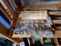 Set of Forstner bits wrapped in plastic inside a wooden case with foam padding inside the lid, placed on wooden shelving.