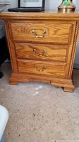 Front view of first bedside table showing three drawers and brass bail pulls