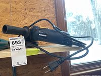 Angle grinder placed on bench near window, showing power cord and side handle.