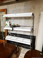 Front view of three-tier chrome metal rack with shelves and two mounted fluorescent grow lights
